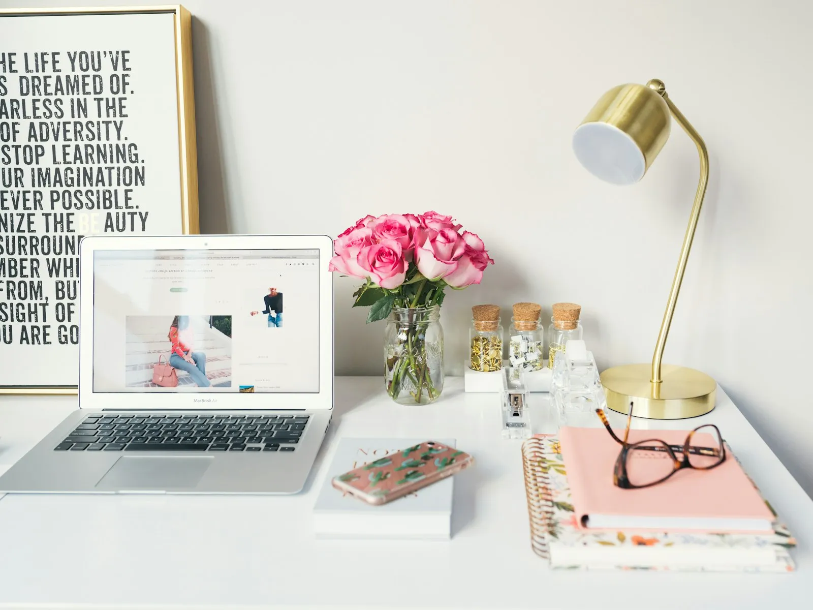 Warm desk setup with a laptop, notebook, lamp, and fresh flowers