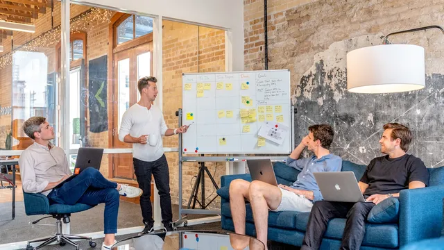 Presenter sketching a plan on a whiteboard while a small team watches