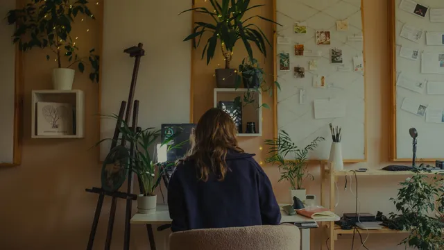 Designer working at a wooden desk in a plant-filled studio
